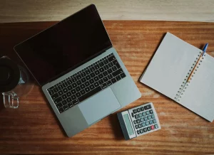 Notebook, calculator, and laptop on a desk, symbolizing payroll complexities in international business operations