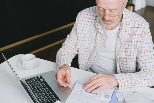 Man reviewing Swiss pension deduction documents while working on a laptop, checking payroll contributions, retirement savings calculations, and employee benefit records in an office environment.